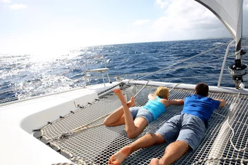 Poster Couple relaxing on catamaran net looking at the sea © goodluz