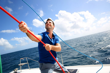 Fototapeta premium Young man lifting the sail of catamaran during cruising