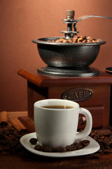 Coffee grinder and cup of coffee on brown background