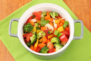 Vegetable stew in gray pot on color napkin on wooden background