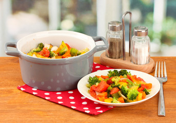 Vegetable stew in gray pot on wooden table on bright background