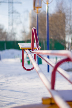 Kids red metal swings on winter playground covered with snow