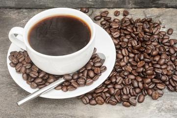 Steaming hot cup of coffee  surrounded by dark coffee beans with