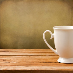 Background with white cup on wooden table over grunge wall