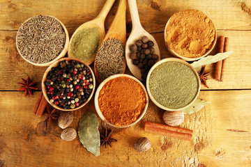 bowls and spoons with spices, on wooden background
