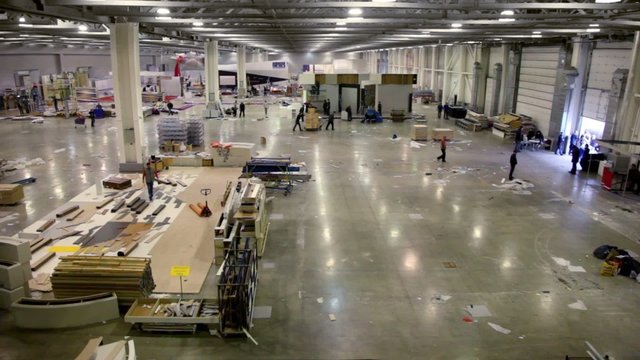 Many people work in large hangar with building materials