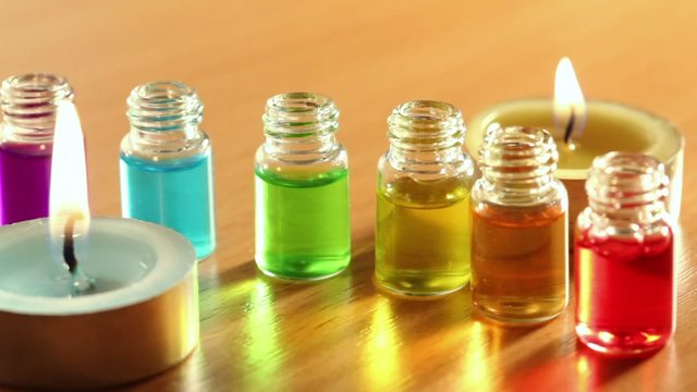 Two candles burns, and six transparent open bottles with color