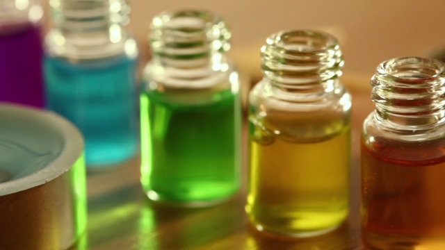 Two candles burn, few open bottles with color aroma oil and sea