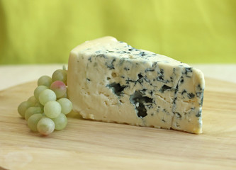 Slice of blue cheese with grapes on green background, close-up