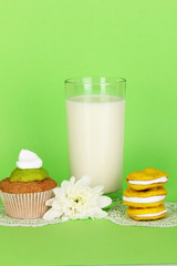 Glass of fresh new milk with cakes on green background