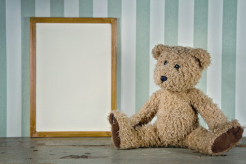 Old teddy bear next to an empty frame