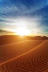 Sandy barkhans in the evening. The sun with beams in the desert.