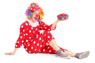 A smiling clown on a floor holding a gift