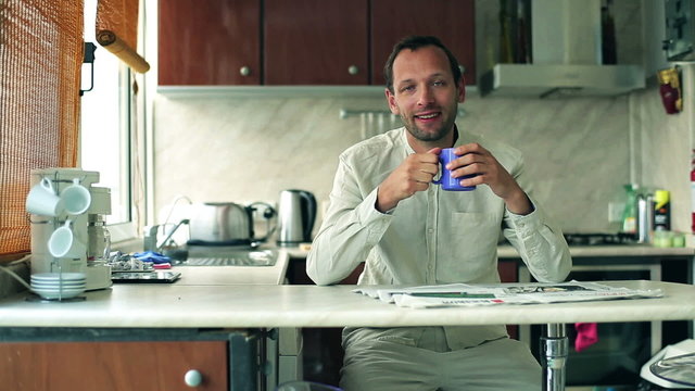 Portrait of smiling man sitting in the kitchen and drinking coff