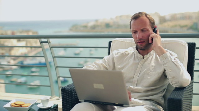 Happy man sitting on the terrace with laptop computer and cellph