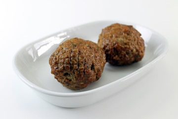 Two meatballs angled on a plate closeup isolated on white