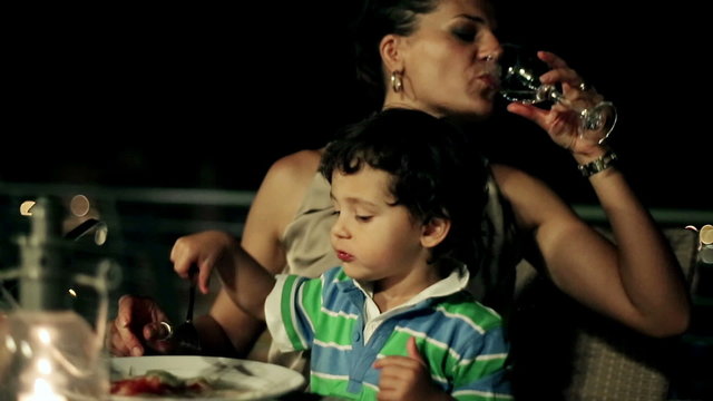 Mother with her son eating dinner on the terrace at night, stead
