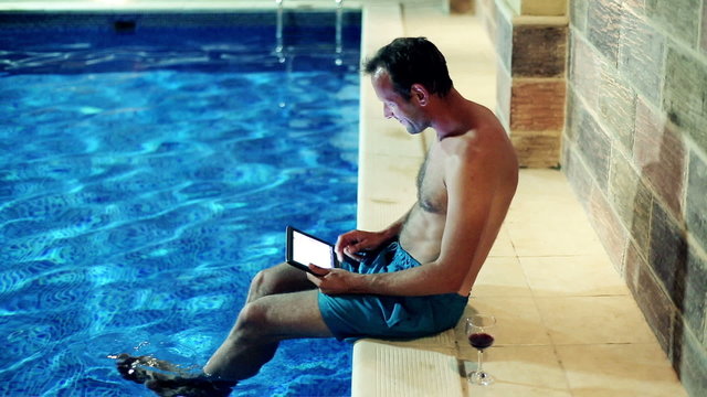 Happy man chatting with tablet computer by the swimming pool at