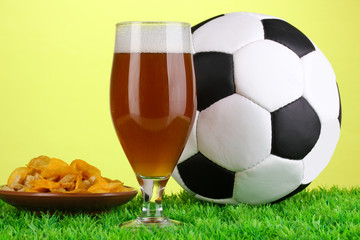 Glass of beer with soccer ball on grass on green background