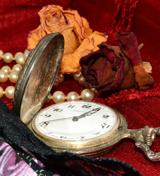 Reloj antiguo de bolsillo con rosas secas collar de perlas y abanico sobre tela granate.