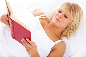 Obraz na płótnie Canvas Attraktive junge Frau liest ein Buch im Bett