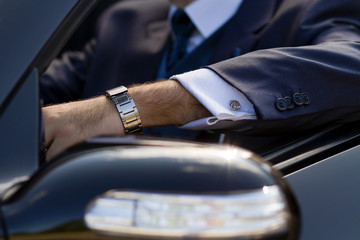 Businessman rides in expensive car wearing suit with cufflinks and luxury watches on wrist
