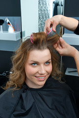 Naklejka premium hair stylist curling woman hair in salon