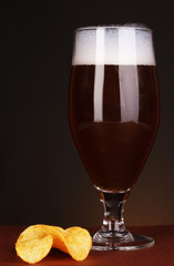 Glass of beer with chips on brown background