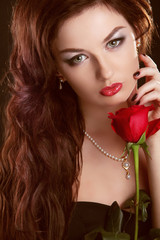 Beautiful brunette woman with red rose and long curly hair
