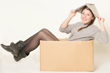 junges Mädchen mit Zeitung auf dem Kopf sitzt in einem Karton