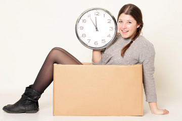 Junges Mädchen mit Uhr in der Hand sitzt im Karton