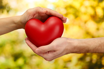 Fototapeta na wymiar Czerwone serce w ręce kobiety i mężczyzny, na zielonym tle