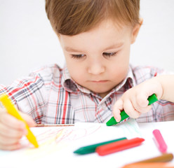Little boy is drawing on white paper
