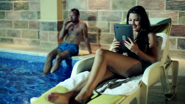 Young couple with tablet computer sitting by the swimming pool a