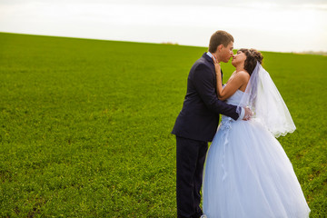 bride and groom outdoor standing in a green field hug, newlyweds