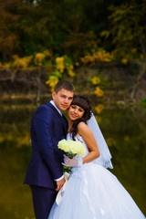 bride and groom standing at the water behind the yellow leaves f