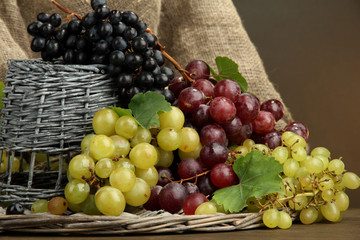 assortment of ripe sweet grapes in basket, on brown background