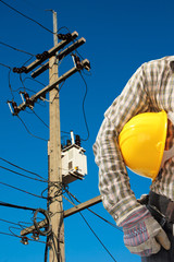 Electrician worker at work against electric post and blue sky ba