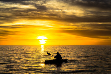 Naklejka na ściany i meble Rybaka w kajaku na oceanie przed dramatycznym zachodzie słońca