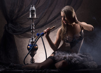 A young and sexy blond woman smoking a hookah