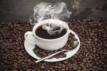 Steaming hot cup of coffee  surrounded by dark coffee beans with