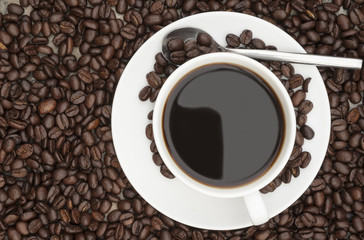 Steaming hot cup of coffee  surrounded by dark coffee beans with