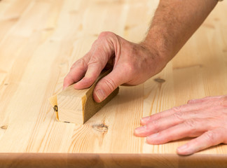 Mans hand on sanding block on pine wood