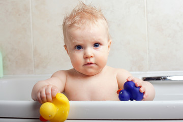 Cute baby girl in a bath holding toy ducks