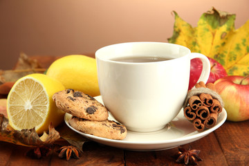 cup of hot tea and autumn leaves, on brown background