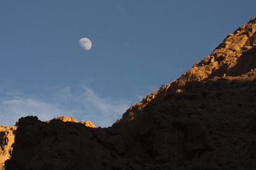 small moon over a mountain cliff in the desert