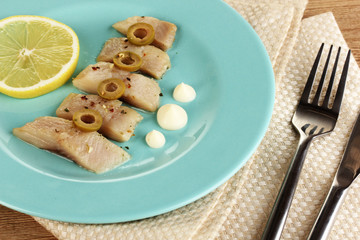 Dish of herring and lemon on plate on wooden table close-up