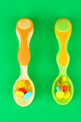 Plastic spoons with color pills, on green background