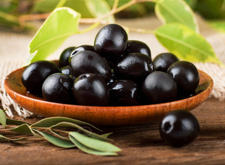 Black olives in a wooden plate and a rough board