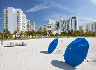 Miami Beach, Florida, sunny summer day, blue umbrellas and lounge chairs with modern architecture buildings. Famous travel location - 48258974